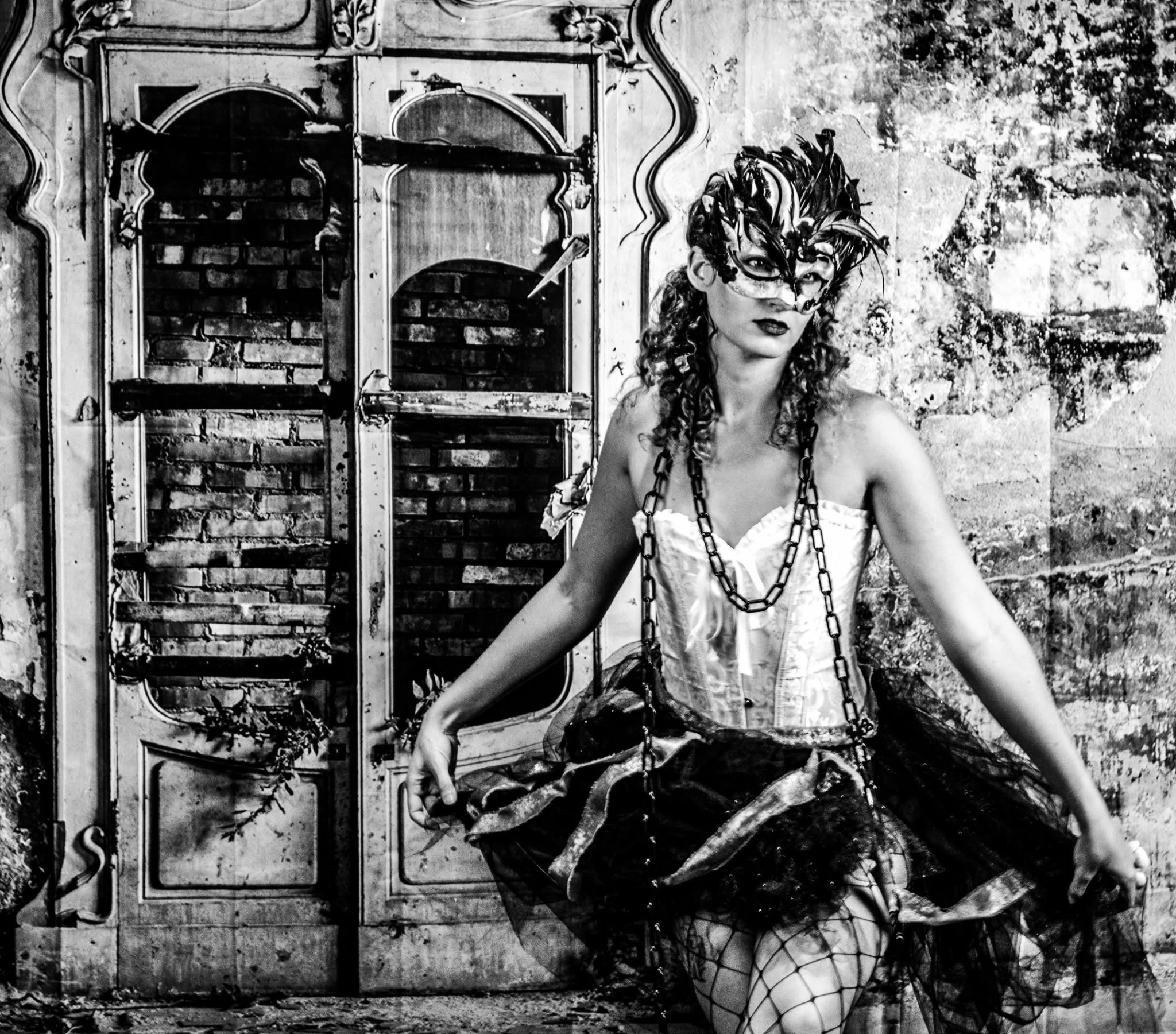 Black-and-white carnival portrait wearing a feather mask, corset, chains, and sculptural skirt