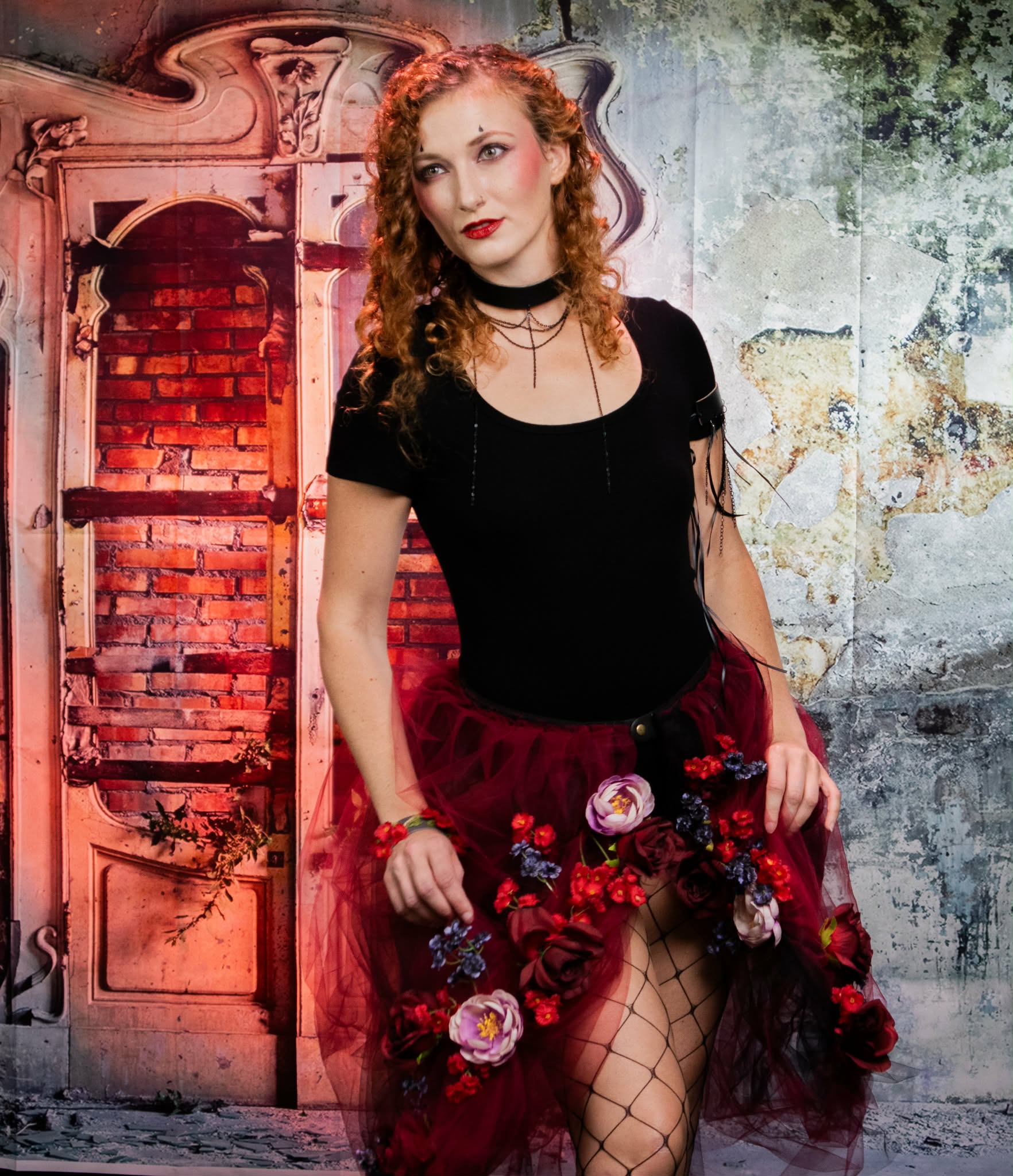 Post-apocalyptic carnival portrait with red floral skirt, layered chain jewelry, and dramatic makeup