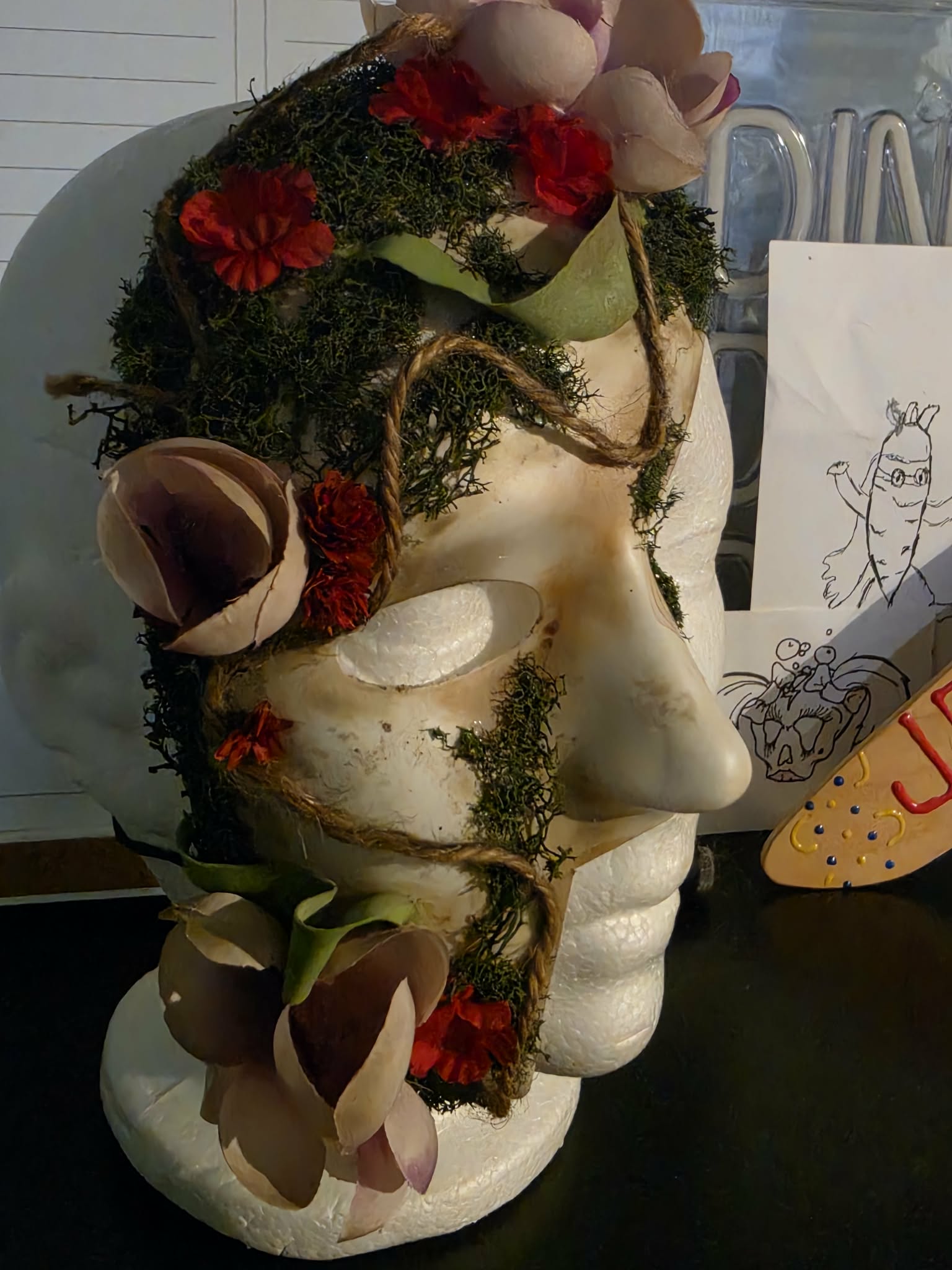 Sculptural skull mask covered in moss, flowers, and botanical details